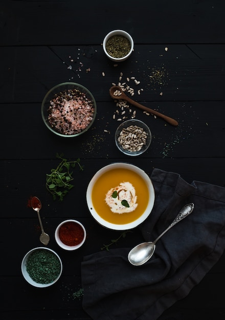 Kürbissuppe mit Sahne, seedsand verschiedenes spicesl in der rustikalen Metallschüssel über Schmutzschwarzem. Ansicht von oben.