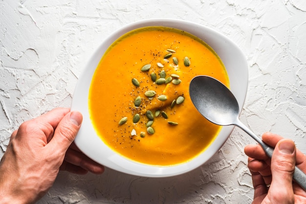 Kürbissuppe mit Samen und einem Löffel in der Hand