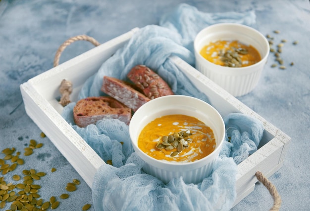 Kürbissuppe mit Samen und Sahne in einer weißen Schüssel in einer Holzkiste auf blauem Hintergrund, selektiver Fokus