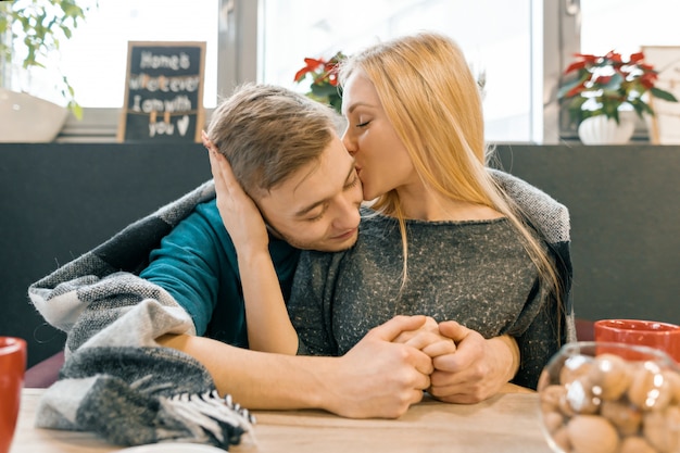 Küssen, die die jungen Paare umfassen, die zusammen im Café unter einer warmen Decke sitzen