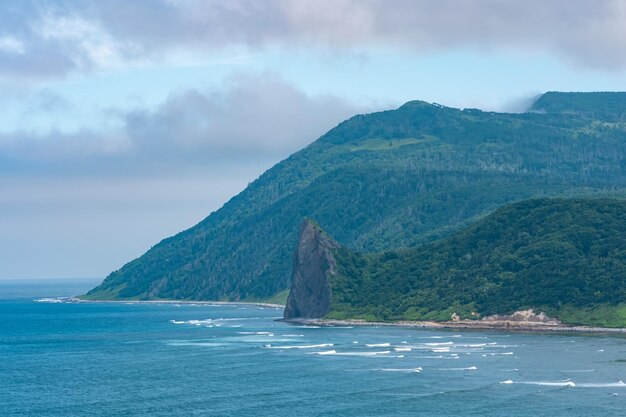 Küste der Insel Kunaschir mit Basaltfelsen und bewaldeten Bergen in den Wolken