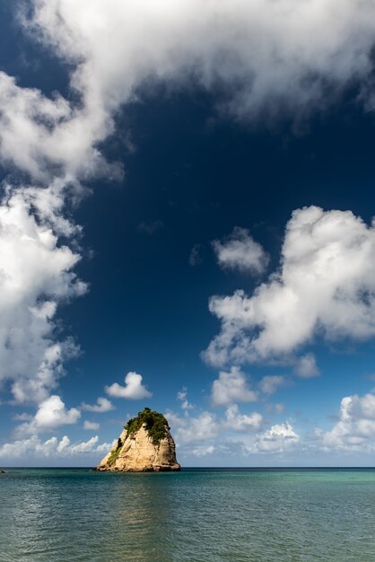 Küstenfelsen isoliert auf dem Meer, umgeben von einer langen vertikalen weißen Wolke in Form von Rauch.