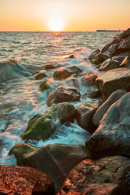 Küstenlandschaft mit warmem Abendlicht, wenn Wellen auf mit Seetang bedeckten Felsen brechen