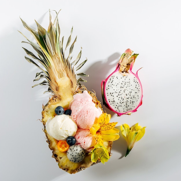 Kugeln aus Eisdekoration Blumen und Beeren in Hälften von Ananas. Sommer tropisches Konzept.