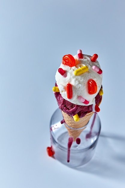 Kugeln von Beeren- und Vanilleeis in einem Waffeltüte mit mehrfarbigen Kapseln in einer Flasche auf einem blauen Hintergrund. Draufsicht