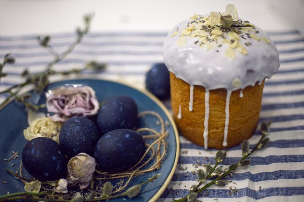 Kulich com design de decoração de esmalte de açúcar ovos de páscoa azuis estão em um prato com um salgueiro em fundo de tecido listrado Paska Easter Bread