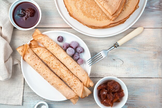 Kulinarische Pfannkuchen mit Füllung und Beeren auf einer hellen Holzoberfläche. Draufsicht mit Platz zum Kopieren. Konzept des Kochens, Maslenitsa.