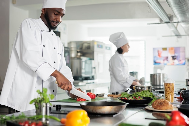 Kulinarischer Experte in der professionellen Restaurantküche kocht ein Gourmetgericht, das abends zum Abendessen serviert wird. Chefkoch schneidet roten Pfeffer, während er köstliches Essen garniert.