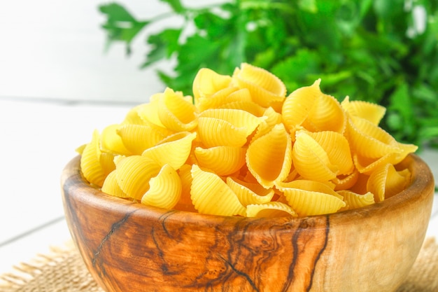 Kulinarischer Hintergrund mit Conchiglie-Teigwaren auf Holztisch. Pasta in Form von Muscheln