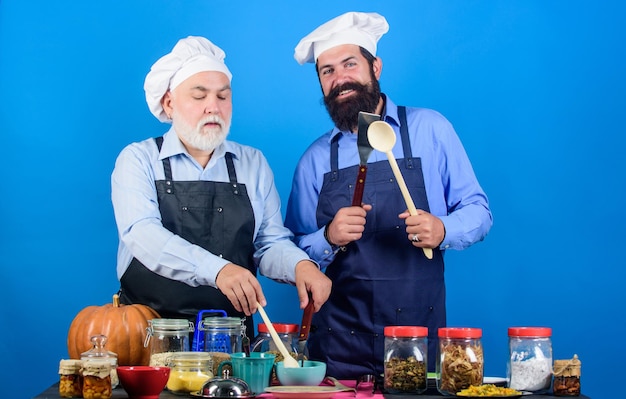 Kulinarisches Buch Ältere bärtige Männer professionelle Restaurantköche Chefkoch Männer kochen Vater und Sohn kulinarisches Hobby Familienrestaurant Ausgewählte Zutaten Hausgemachte Mahlzeit Essen zubereiten Kulinarisches Rezept