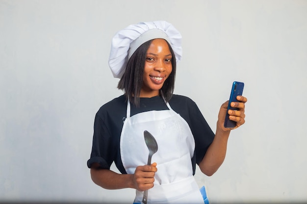 Kulinarisches und Leutekonzept kochen Glücklicher lächelnder weiblicher Chef in der Haube und in der Jacke mit Telefoncomputer über weißem Hintergrund