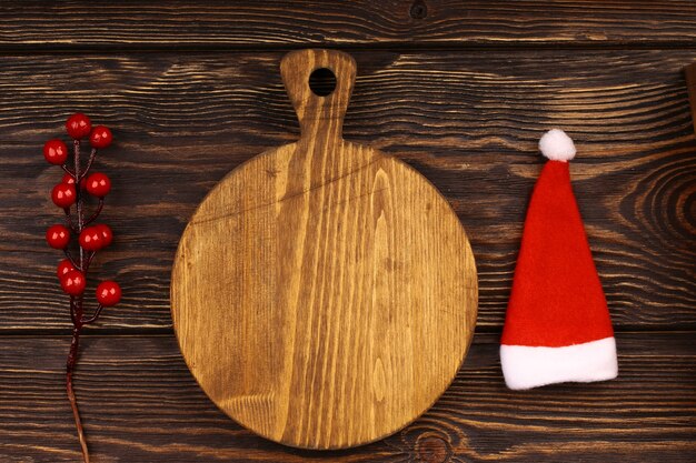 Kulinarisches Weihnachtslayout auf einem hölzernen Hintergrund. Holzschneidebrett mit Weihnachtsartikeln für das Feiertagstischmenü. Ansicht von oben, flacher Stil.