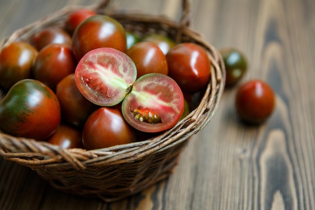 Kumato - variedade escura de tomate - em tigela de salgueiro trançado feito à mão sobre o fundo de madeira escura