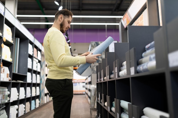 Kunde in einem Geschäft für Wandvinyltapeten, der eine Röhre mit Wandtapeten aus Papier hält