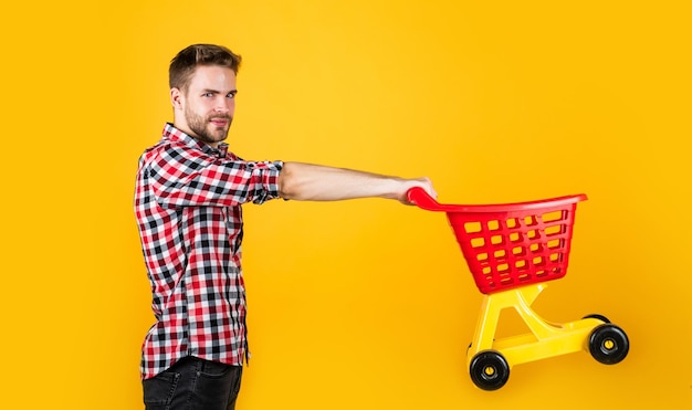 Kunde schiebt Warenkorb Käufer im Supermarkt leeren Spielzeugwagen Mann einkaufen gehen lustiger Mann mit kleinem Einkaufswagen Wochenende beim Kauf von Produkten freut sich über erfolgreiche Einkäufe gibt unklug Geld aus