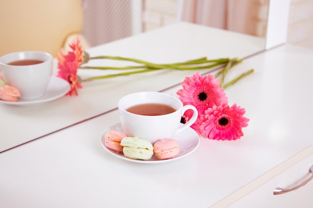 Kundenplatz im Friseur- und Schönheitssalon mit Tasse Tee, Makronen und rosa Gerbera