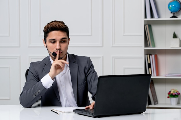 Kundenservice hübscher Herr mit Computer im grauen Büroanzug mit Schweigegeste