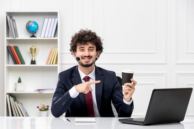 Kundenservice hübscher junger Mann im Büroanzug mit Laptop und Headset lächelnd mit Kaffeetasse