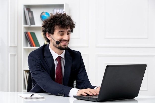 Kundenservice hübscher junger Mann im Büroanzug mit Laptop und Headset lächelnd und tippend