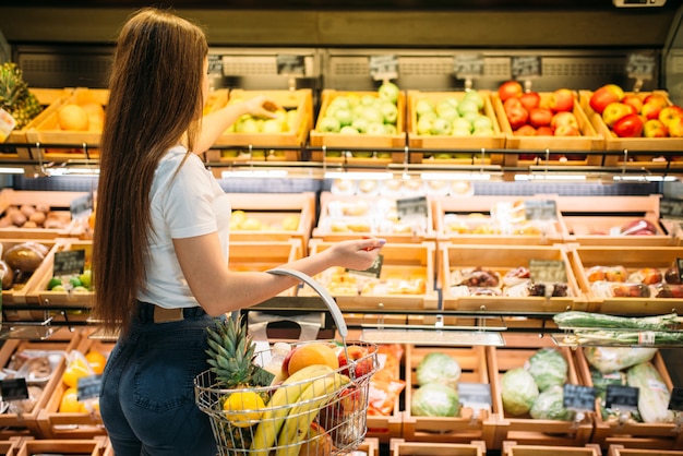 Kundin mit Korb gegen Obstabschnitt im Lebensmittelgeschäft. Frau, die im Supermarkt einkauft