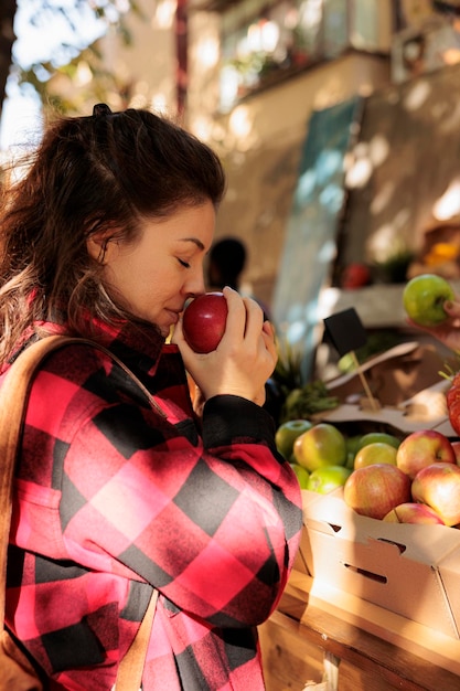 Kundin riecht Äpfel und kauft auf dem Bauernmarkt ein, Käuferin steht am Marktstand und wählt lokal angebautes frisches Bio-Obst und Gemüse aus. Besuch des Erntefests.
