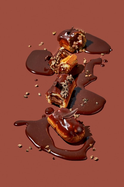 Kunst mit einem Eclair Zerbrochenes Eclair in Pfützen aus Zuckerguss auf braunem Hintergrund Konzeptionelles monochromes Lebensmittelposter für Pistazien-Profiteroles