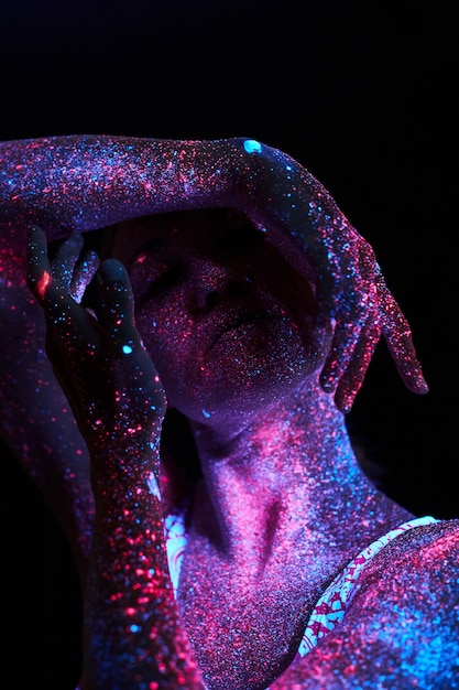 Kunstfrauenkosmos im ultravioletten Licht. Der gesamte Körper ist mit farbigen Tröpfchen bedeckt. Mädchen posiert im Dunkeln. Rauschen, unscharf