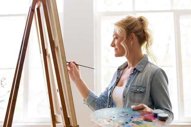 Kunstschule, Kreativität und Menschen Konzept - glückliche lächelnde Frau Künstlerin mit Staffel, Pinsel und Palette Malerei im Studio