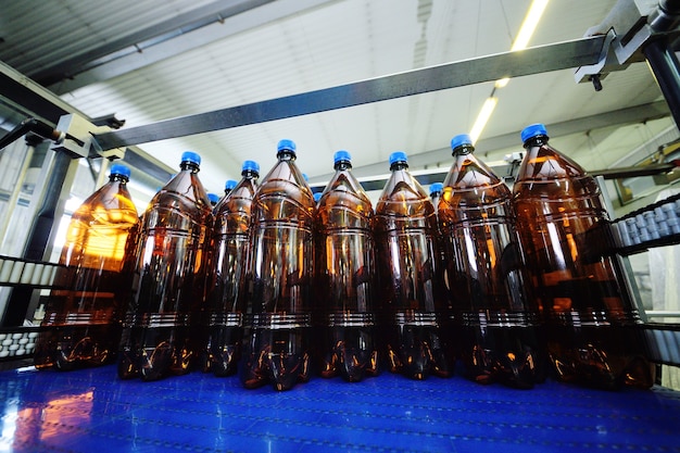 Kunststoff-PET-Flaschen aus gelbem Kunststoff mit blauen Deckeln mit Bier oder süßen Getränken auf einem Förderband im Hintergrund der Fabrik. Industrielle Lebensmittelproduktion von Getränken.