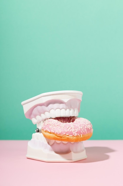 Kunststoffbacken halten süßen rosa Donut in den Zähnen Zahngesundheit Zahnheilkunde und Karieskonzept