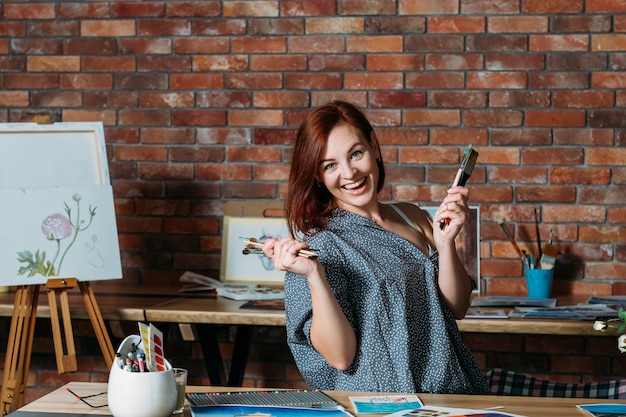 Kunsttherapie. Stressabbau Studioatmosphäre. Lächelnde rothaarige Frau, die mit Pinseln aufwirft.