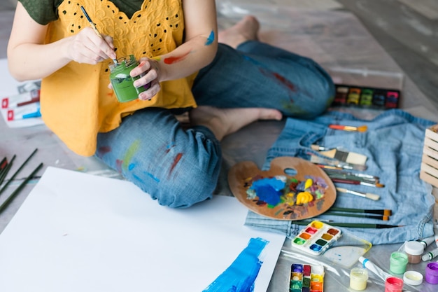Kunsttherapie und Freizeit Zugeschnittene Draufsicht auf eine Dame, die auf dem Boden sitzt und das Malen genießt Palettenpinsel-Set-Organisator