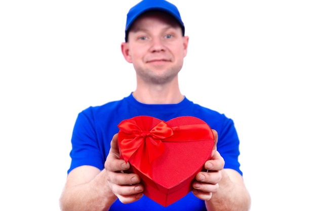 Kurier in blauer Uniform hält eine rote herzförmige Geschenkbox zum Valentinstag. Lieferung nach Hause von