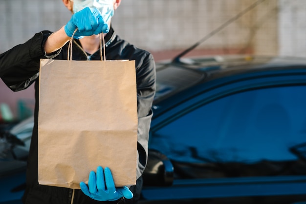 Kurier in schutzmaske, medizinische handschuhe liefern essen zum mitnehmen. mitarbeiter halten kartonpaket. platz für text. lieferservice unter quarantäne, 2019-ncov, pandemisches coronavirus, covid-19.