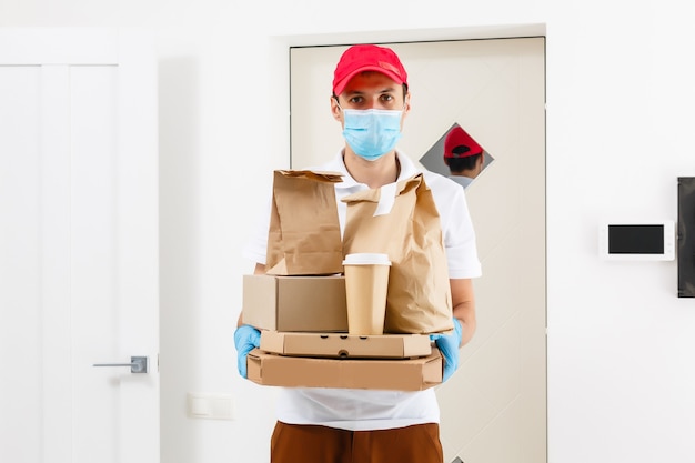 Kurier in Schutzmaske und medizinischen Handschuhen liefert Essen zum Mitnehmen. Lieferservice unter Quarantäne, Krankheitsausbruch, Coronavirus Covid-19-Pandemiebedingungen.