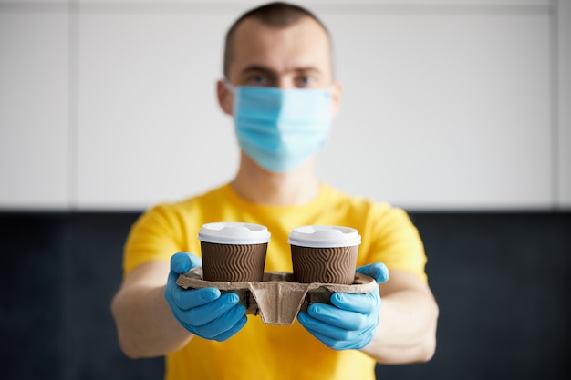 Kurier in Schutzmaske und medizinischen Handschuhen liefert Essen zum Mitnehmen und Kaffee. Lieferservice unter Quarantäne, Krankheitsausbruch, Coronavirus-Covid-19-Pandemie.