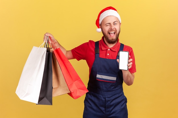 Kurier in Weihnachtsmann-Hut mit Einkaufstüten und Smartphone mit leerem Display