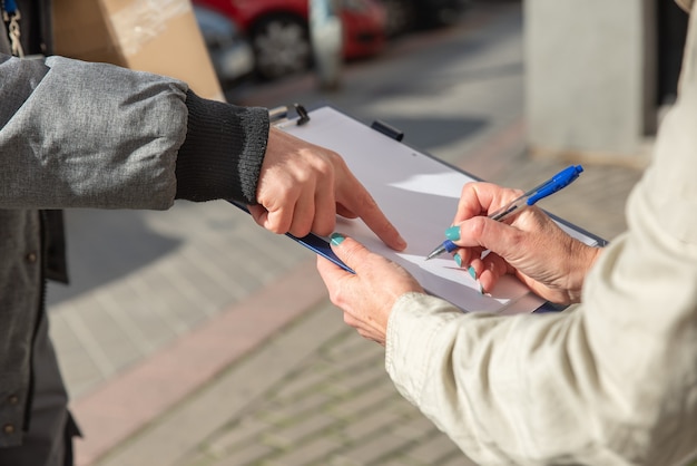 Kurier liefert Bestellung an Frau, die für die Lieferung des Pakets unterschreibt, aus nächster Nähe