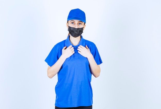 Kurierin in Maske und blauer Uniform zeigt auf sich.