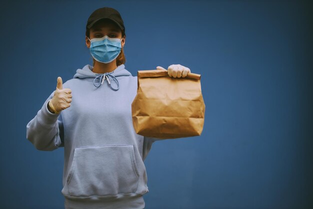 Kuriermädchen in einer medizinischen Maske und medizinischen Handschuhen auf blauem Hintergrund Vintage-Fotoverarbeitung