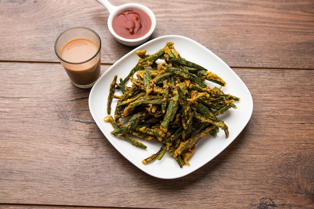 Kurkuri Bhindi oder knuspriger Ladyfinger oder Okra Fry Rezept, serviert in einer Schüssel mit Ketchup und heißem Tee. selektiver Fokus