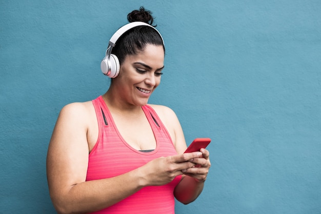 Kurvige Frau, die nach dem Joggen im Freien Playlist-Musik mit dem Handy hört - Fokus auf Gesicht