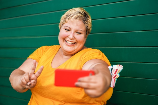 Kurvige Frau, die selfie mit Handy im Freien nimmt