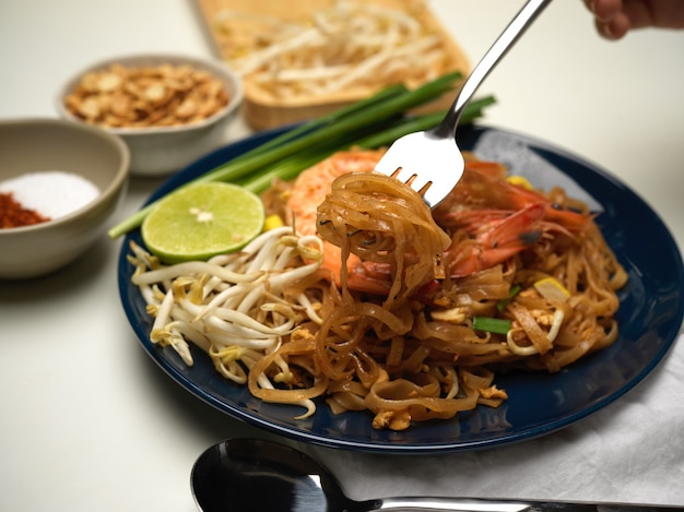 Kurzer Schuss der Frau, die Pad Thai isst, gerührte thailändische Nudeln mit Garnelen rührt, die auf schwarzem Teller mit Limette, Sprossen und Schnittlauch dienen