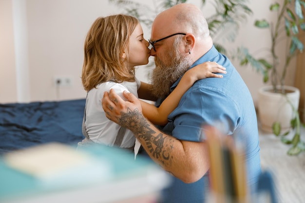 Kurzhaariges kleines Mädchen umarmt und küsst die glückliche Vaternase, die zu Hause auf dem Bett sitzt