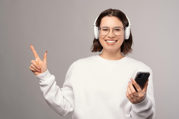 Kurzhaariges Mädchen mit Kopfhörern zeigt beiseite, während es das Telefon hält