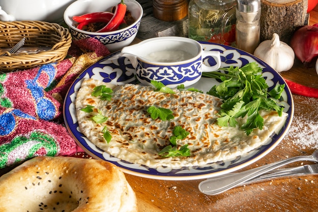 Kutab com verduras. Pão fino fino feito de massa sem fermento com cebolinha, endro, azeda, espinafre, coentro e molho Matzoni em um prato tradicional uzbeque