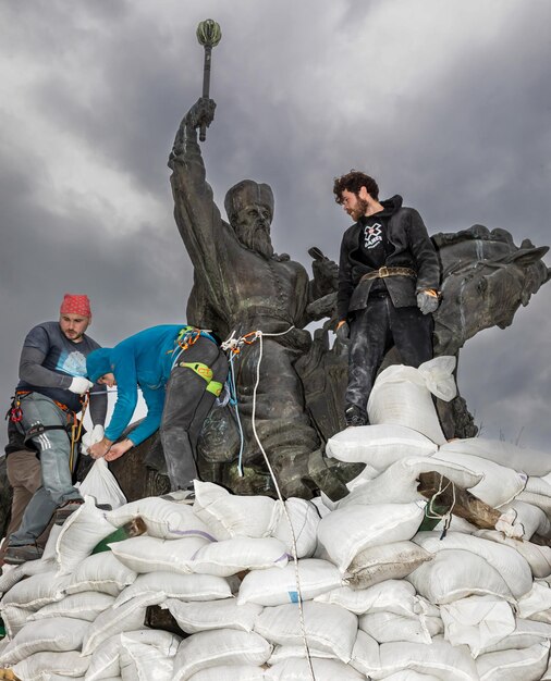 KYIV UCRÂNIA 26 de março de 2022 Monumento a Hetman Sahaidachny com sacos de areia para proteger contra bombardeios russos em Kiev Um grupo de jovens cobre o monumento com sacos de areia