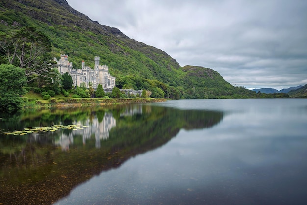 Kylemore Abbey in Connemara, County Galway, Irland mit Spiegelungen im Pollacapall Lough. Kylemore Abbey ist ein Benediktinerkloster, das 1920 auf dem Gelände von Kylemore Castle gegründet wurde.