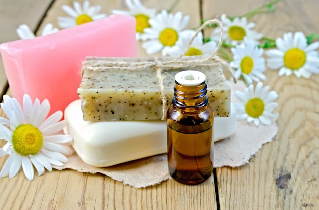 Öl in einer Flasche, hausgemachte Seife auf einem Stück Papier, Gänseblümchenblumen auf einem Hintergrund von Holzbrettern